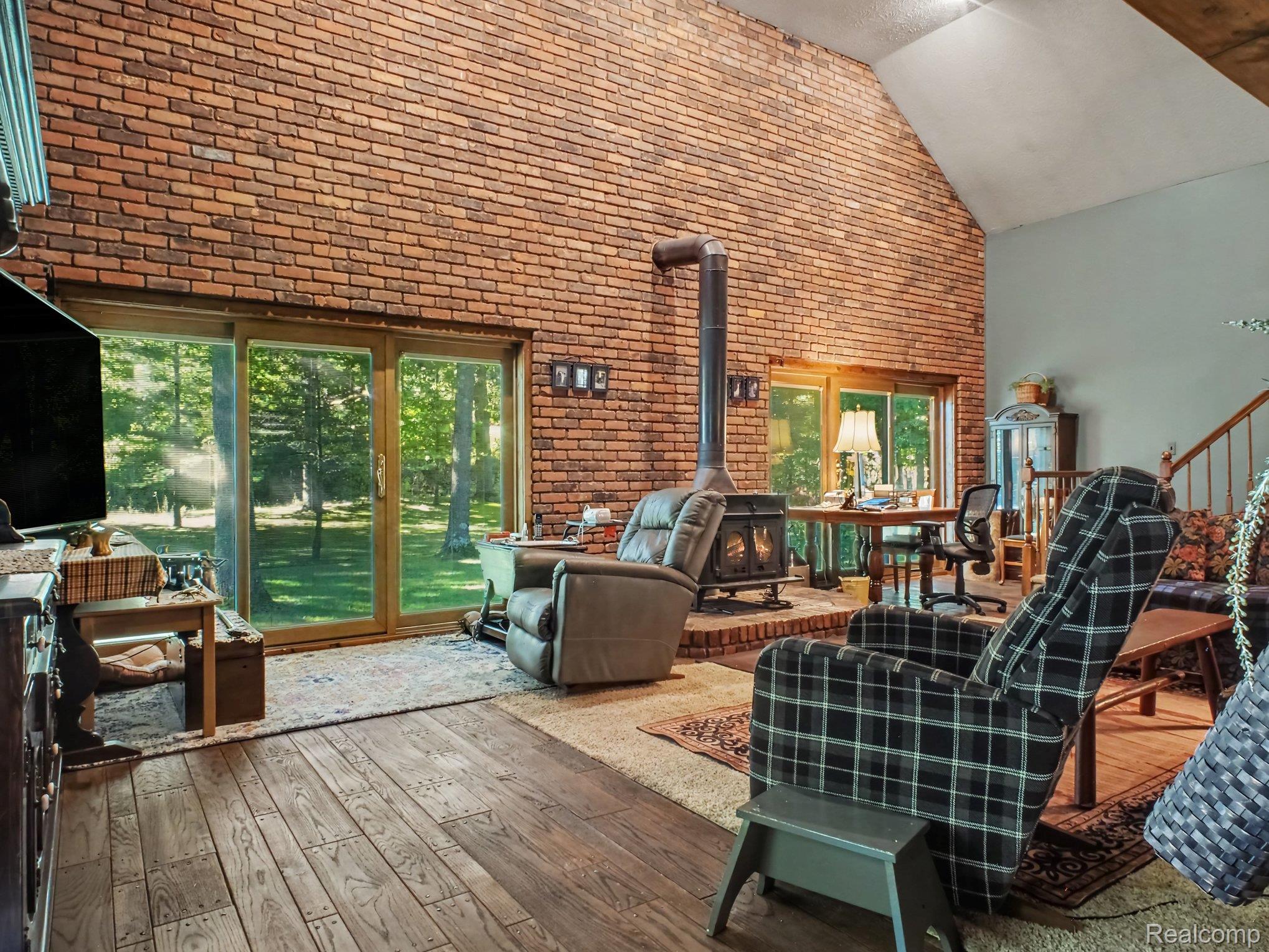 3284 Pratt Road Metamora, MI 48455 - Photo 11 of 22 Vaulted ceiling with a brick accent wall, wood-finish flooring, and a free-standing wood-burning stove