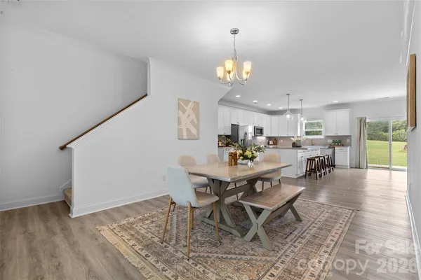 a view of a dining room and livingroom with furniture wooden floor a rug a painting and a chandelier