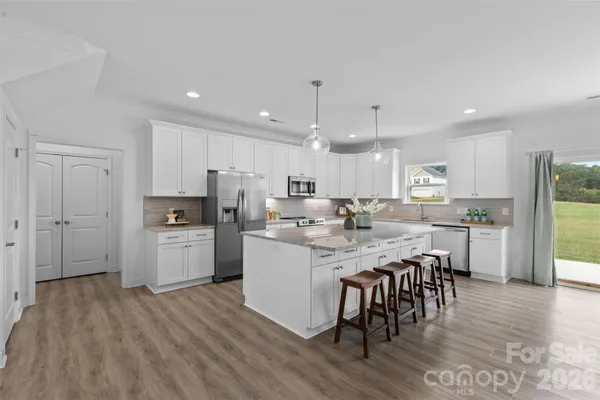 a kitchen with a white table chairs a sink dishwasher a refrigerator and cabinets with wooden floor
