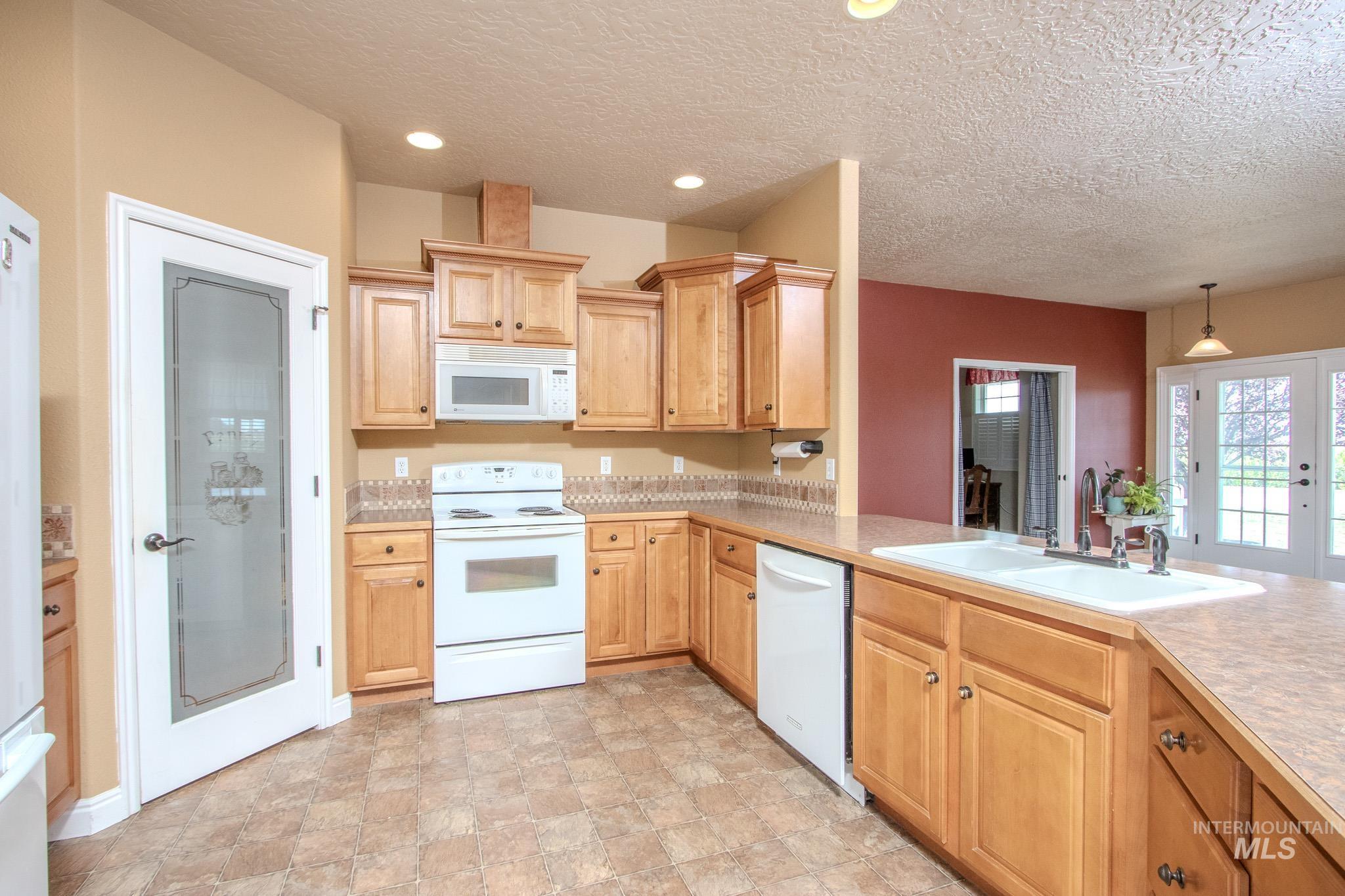 13569 Midway Road Nampa, ID 83651 - Photo 9 of 25 Kitchen featuring white appliances, a textured ceiling, light countertops, stone finish floors, and light brown cabinetry