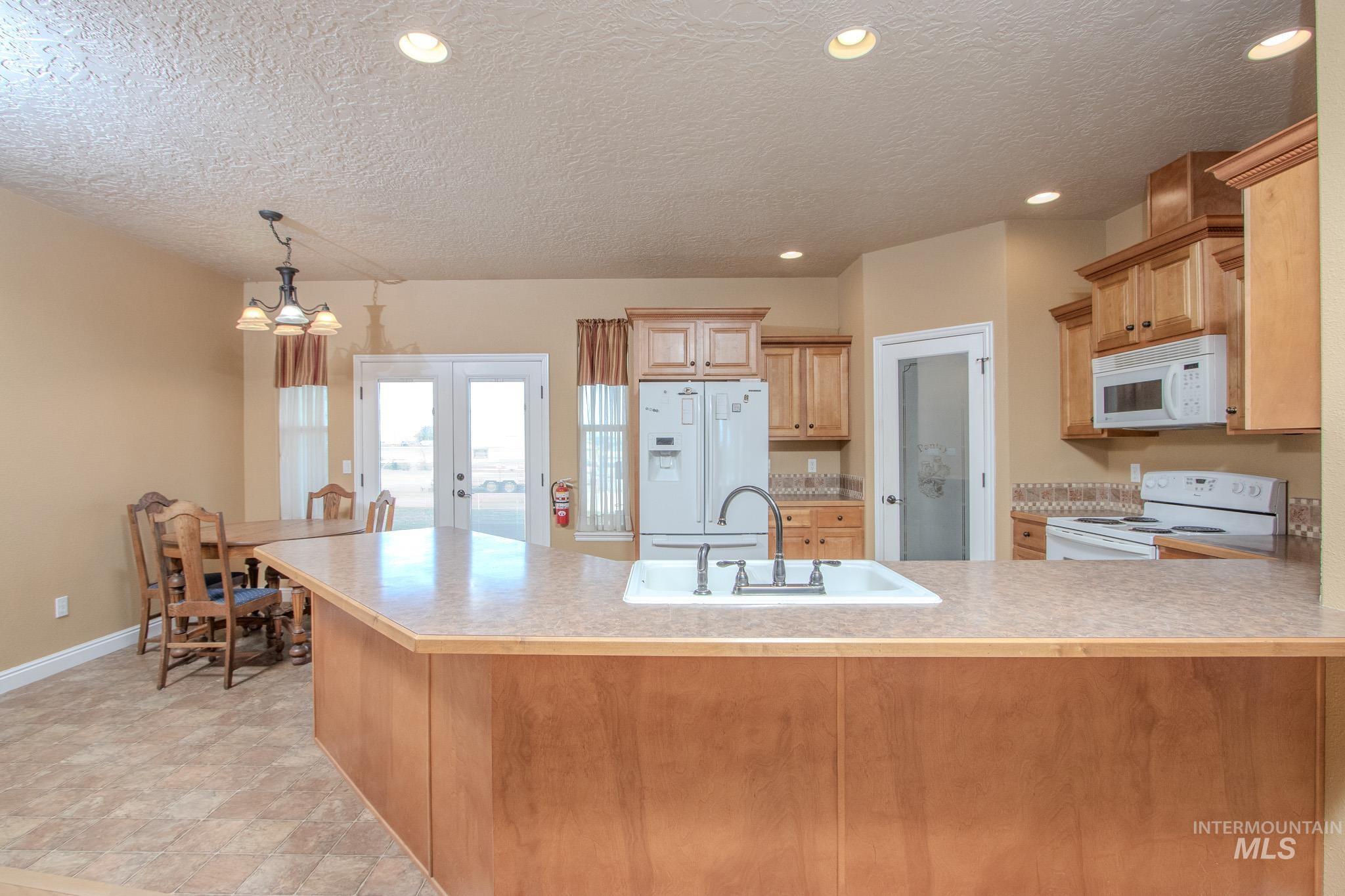13569 Midway Road Nampa, ID 83651 - Photo 10 of 25 Kitchen with french doors, white appliances, a textured ceiling, light countertops, and a peninsula