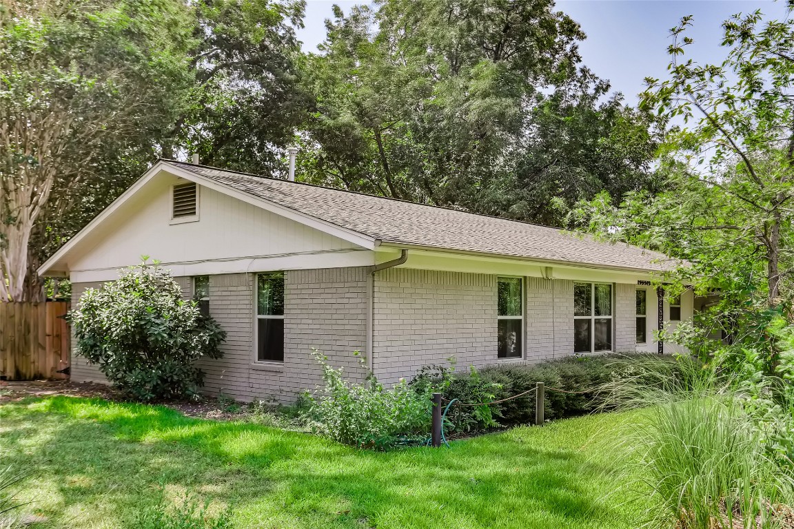 View of property exterior with brick siding, a shingled roof, and view of wooded area