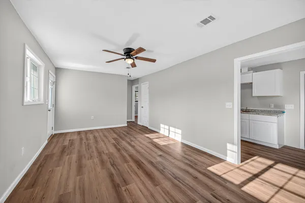 a view of empty room with wooden floor and kitchen view