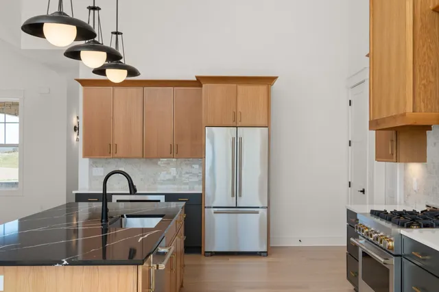 a kitchen with stainless steel appliances granite countertop a refrigerator a sink and a stove with wooden floor