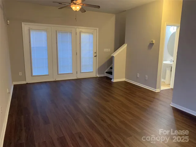 a view of an empty room with wooden floor and a ceiling fan