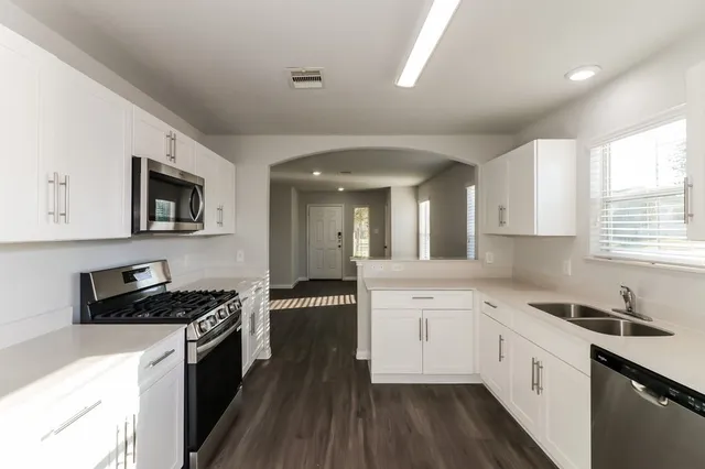 a kitchen with granite countertop a stove top oven a sink dishwasher and white cabinets with wooden floor