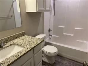 a bathroom with a granite countertop bathtub sink vanity mirror and toilet