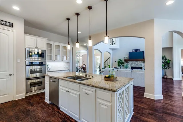 a kitchen with stainless steel appliances kitchen island granite countertop a stove a refrigerator a sink a dining table and chairs with wooden floor