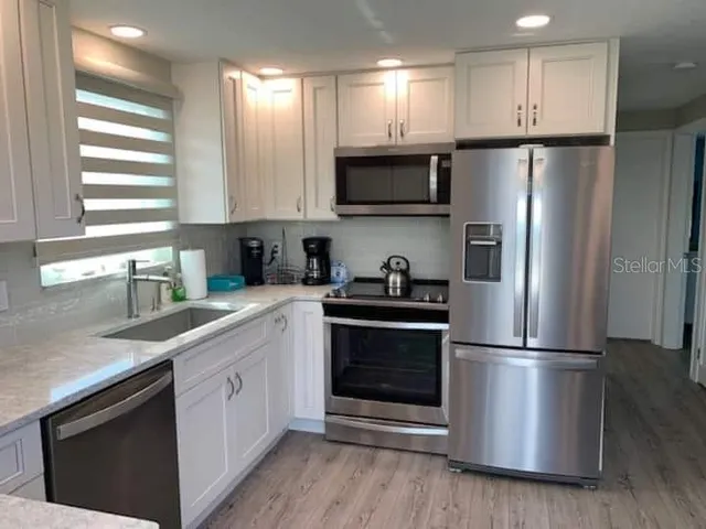 a kitchen with stainless steel appliances granite countertop a refrigerator a sink a stove a microwave and wooden floors