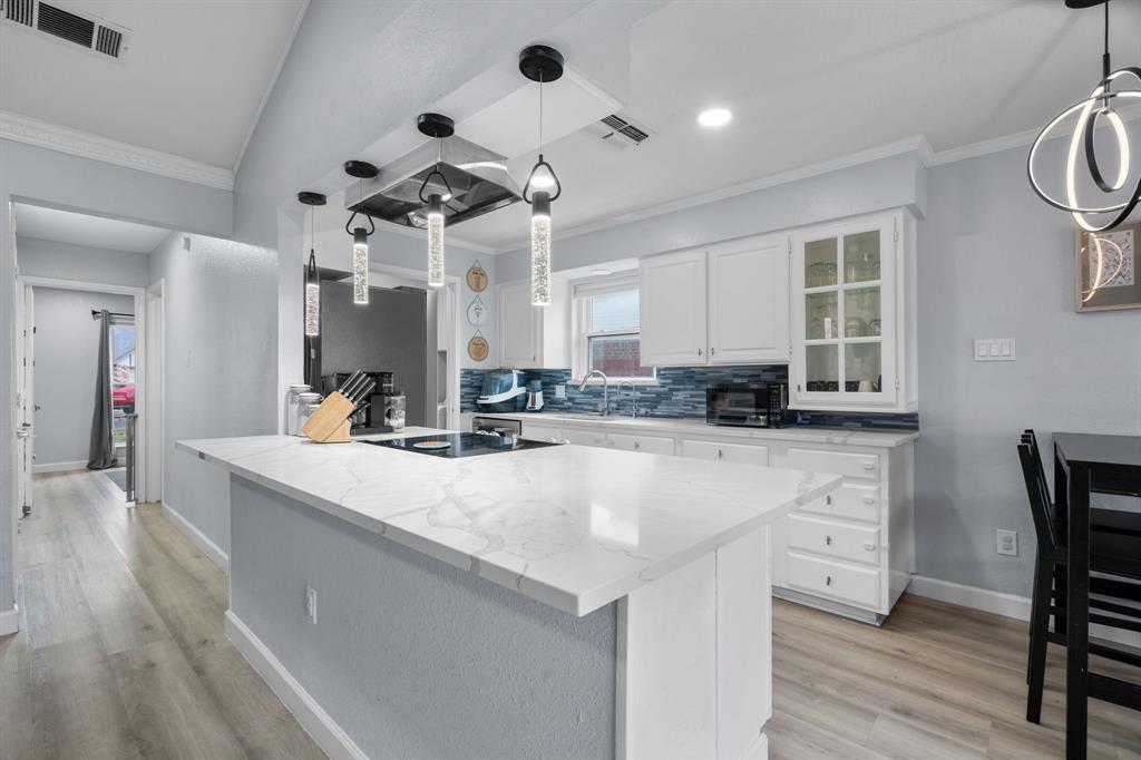 7629 Cedarhill Road Watauga, TX 76148 - Photo 25 of 33 Modern kitchen featuring a large central island with a cooktop, white cabinetry, a blue tile backsplash, recessed lighting, and wood-finish flooring