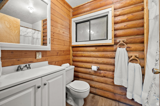 4725 Pine Ridge Road Evanston, UT 82930 - Photo 27 of 82 Bathroom featuring log-style wood paneling, a white vanity with an integrated sink, a built-in mirrored medicine cabinet, a toilet, and a window with a wood frame