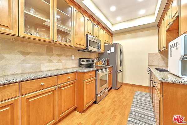 a kitchen with stainless steel appliances granite countertop a refrigerator a oven and white cabinets with wooden floors