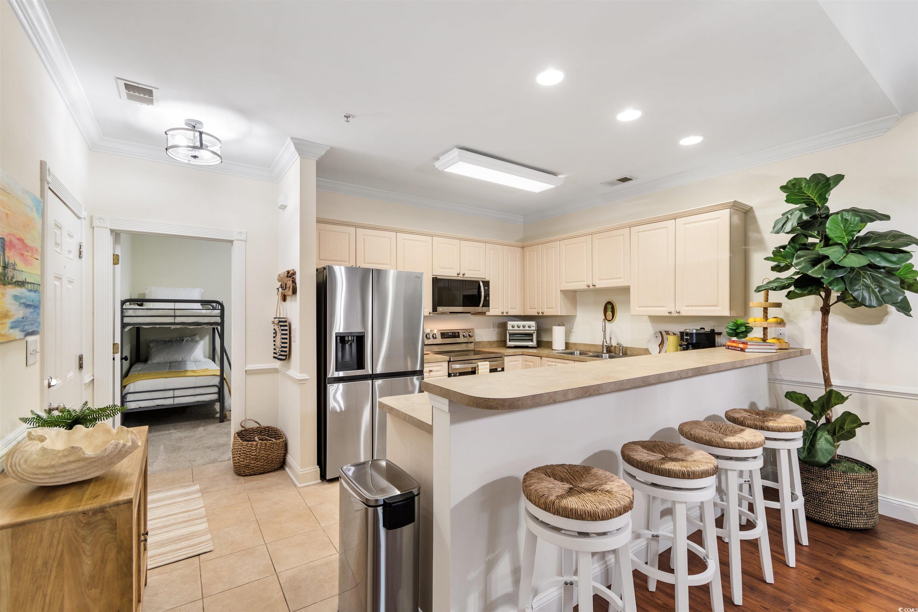 4843 Luster Leaf Circle, Unit 402 Myrtle Beach, SC 29577 - Photo 2 of 33 Kitchen with appliances with stainless steel finishes, cream cabinetry, ornamental molding, a kitchen bar, and recessed lighting