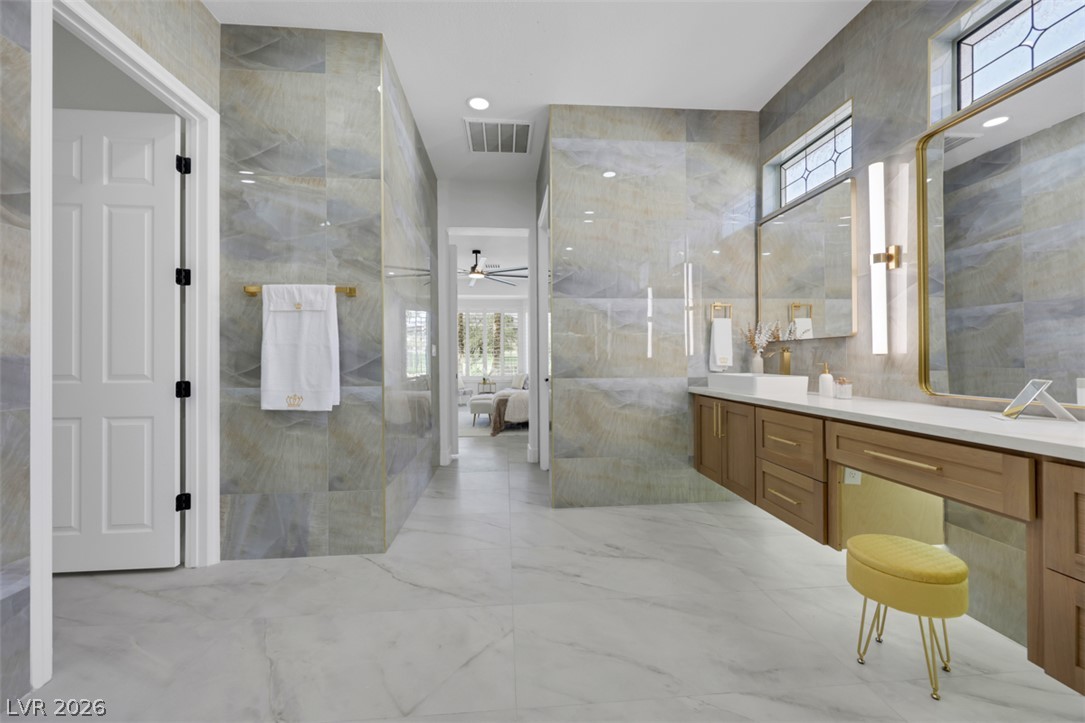 5015 Rivedro Street Las Vegas, NV 89135 - Photo 14 of 91 Marble-look tile flooring and walls create a pristine, well-lit bathroom with sleek vanity cabinetry and modern fixtures.