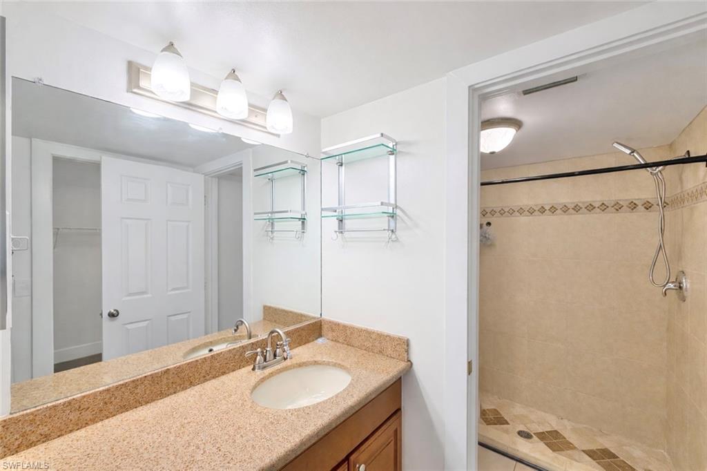 534 Augusta Boulevard, Unit E104 Naples, FL 34113 - Photo 11 of 26 a bathroom with a granite countertop sink a mirror and a shower