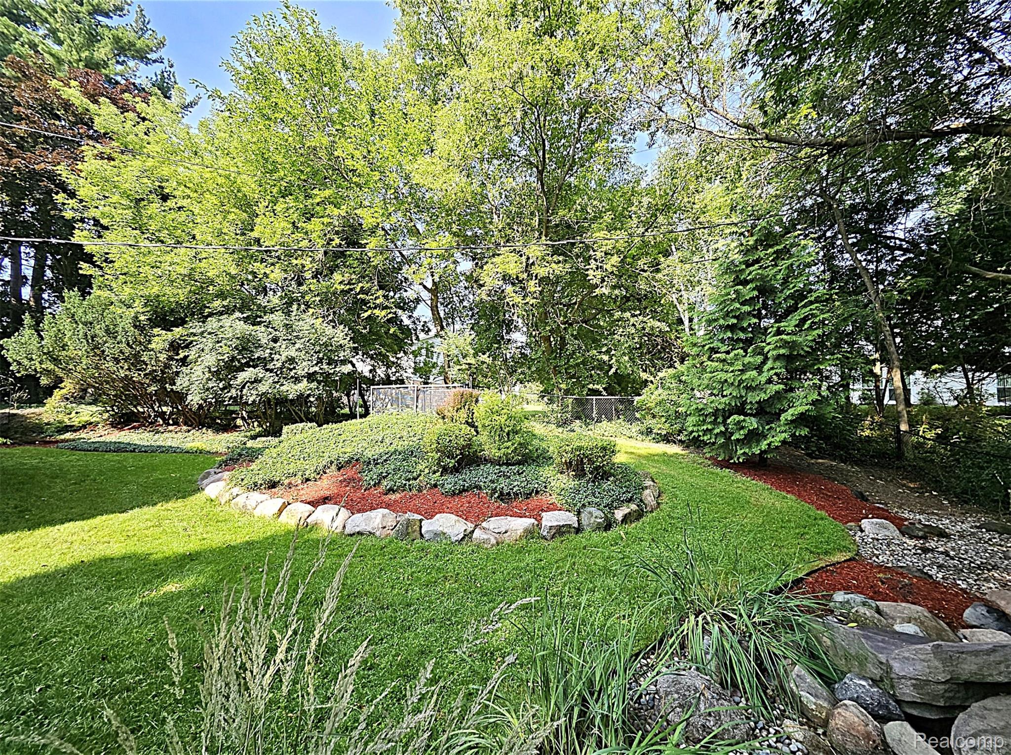 7120 Pebblecreek Road West Bloomfield, MI 48322 - Photo 10 of 31 Lush green lawn with a rock-lined garden bed featuring red mulch and diverse plantings
