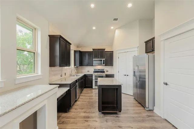 a large kitchen with stainless steel appliances granite countertop a stove a sink dishwasher a refrigerator and a oven with wooden floors