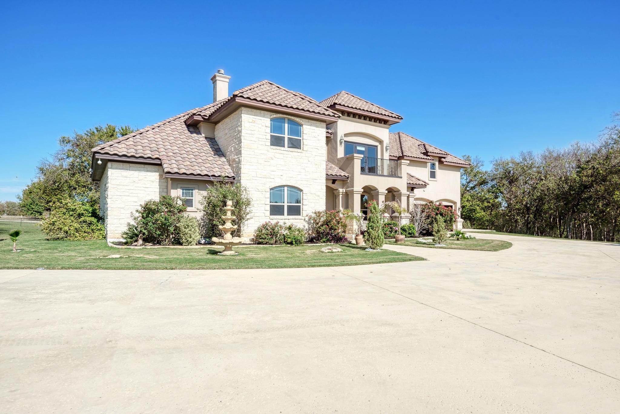 104 Spring Valley Street Hutto, TX 78634 - Photo 4 of 40 Mediterranean / spanish-style house with stone siding, a balcony, a chimney, driveway, and a front lawn