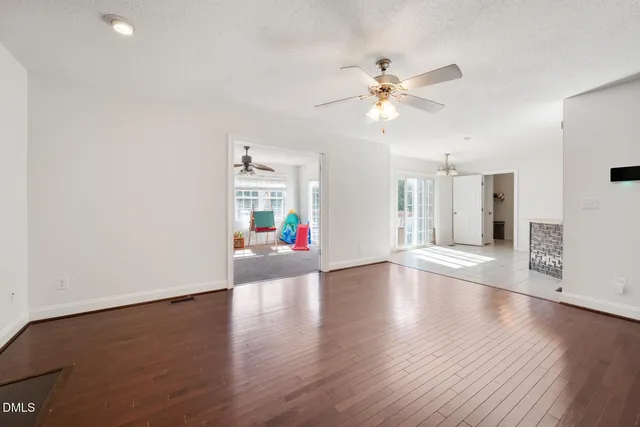 a view of an empty room with wooden floor and a ceiling fan