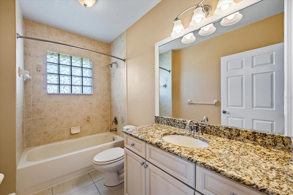 136 175th Avenue East Redington Shores, FL 33708 - Photo 24 of 40 a bathroom with a granite countertop sink a toilet a mirror a bathtub and shower