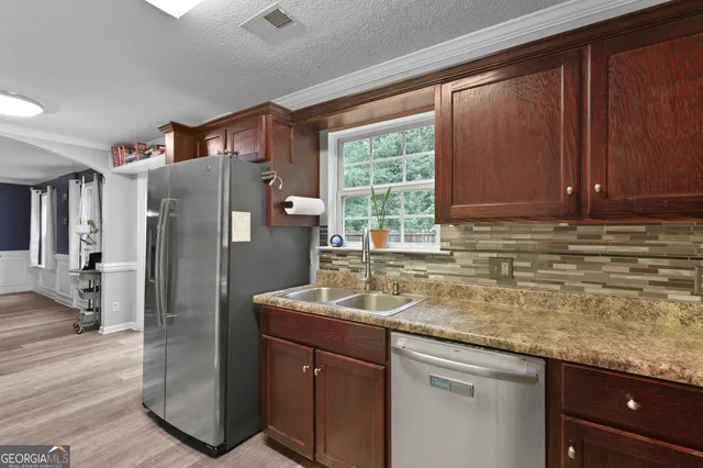 a kitchen with stainless steel appliances granite countertop a refrigerator a sink dishwasher and wooden cabinets with wooden floor