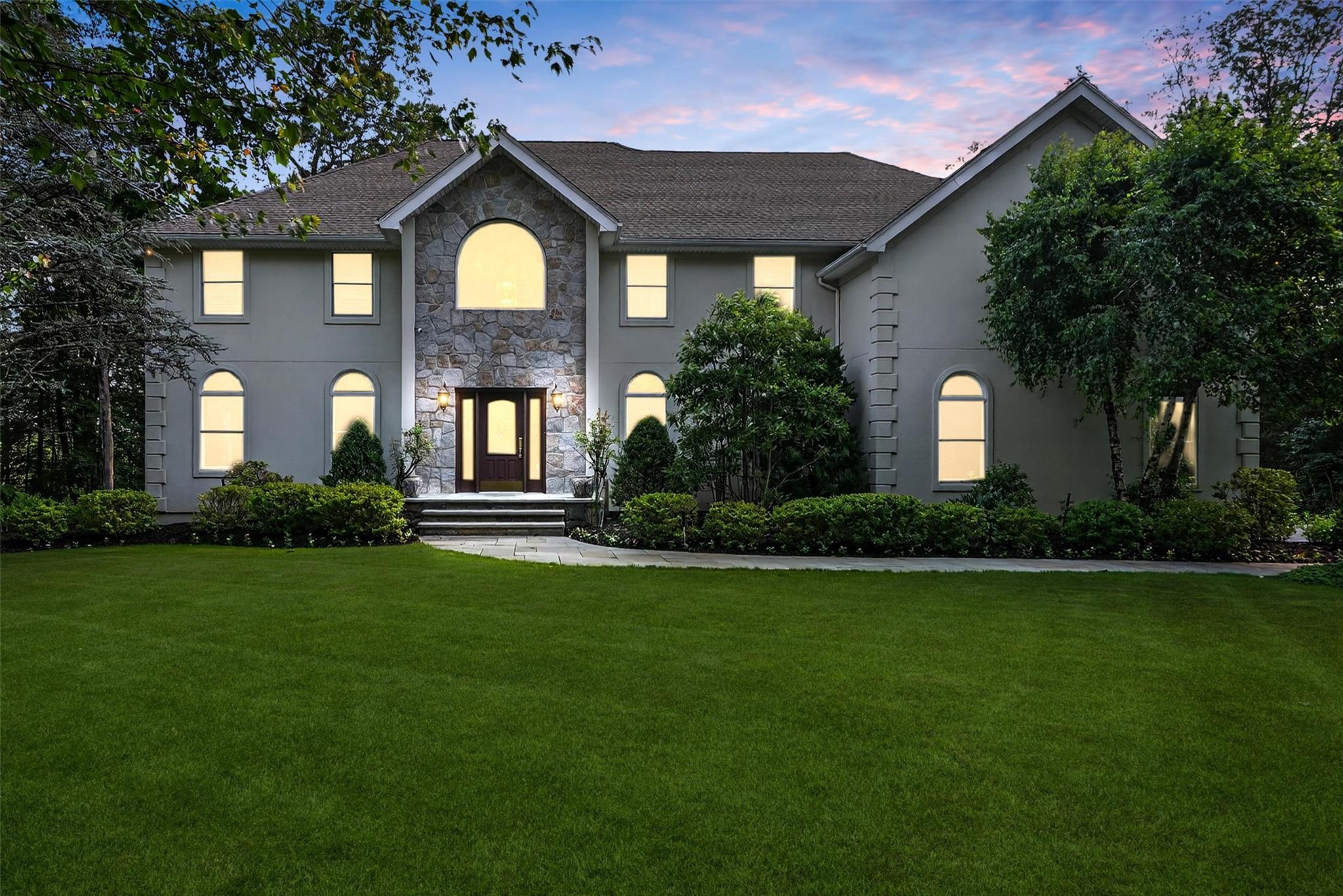View of front of property featuring stucco siding, a lawn, and stone siding
