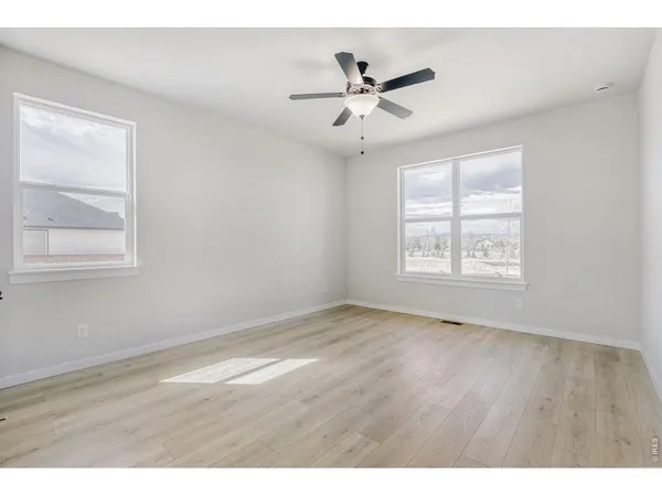 an empty room with wooden floor windows and fan