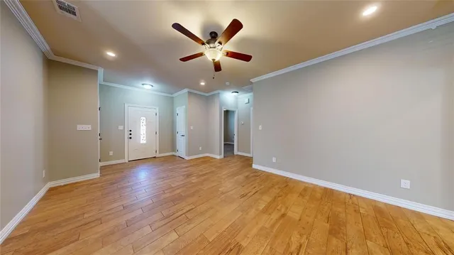 a view of an empty room with wooden floor and a ceiling fan