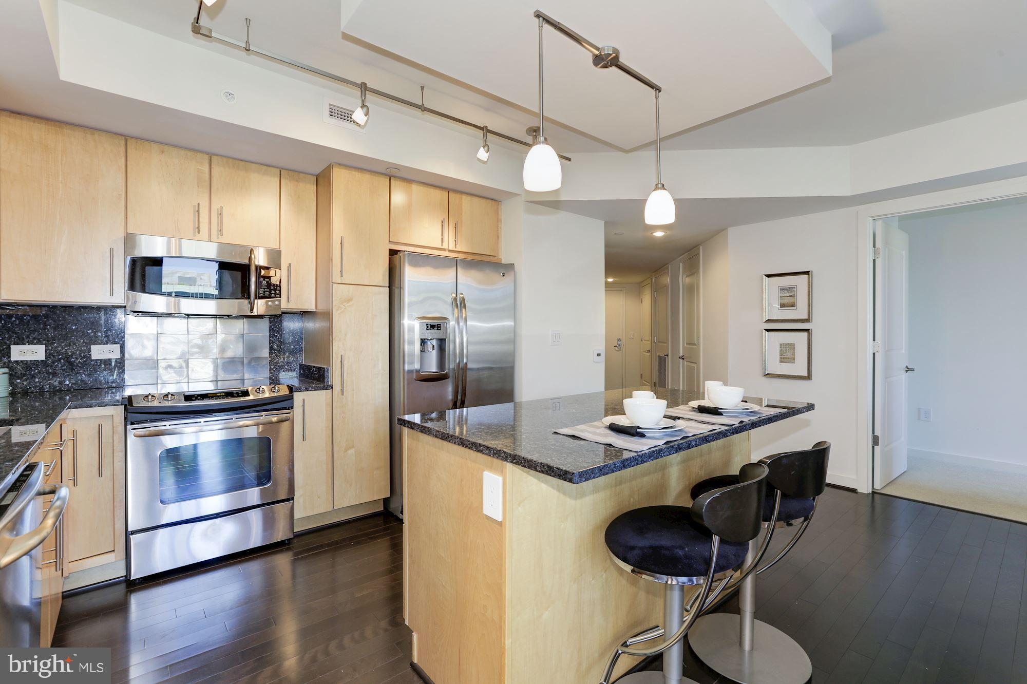 1025 First Street Southeast, Unit 916 Washington, DC 20003 - Photo 10 of 30 a kitchen with stainless steel appliances granite countertop a stove a refrigerator a sink a dining table and chairs with wooden floor