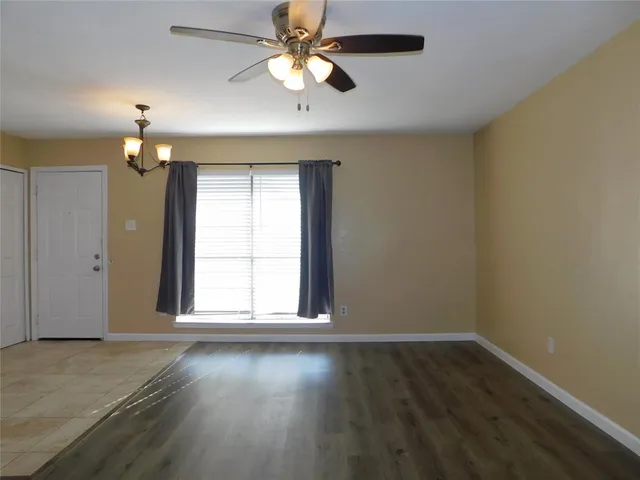 an empty room with wooden floor chandelier fan and windows