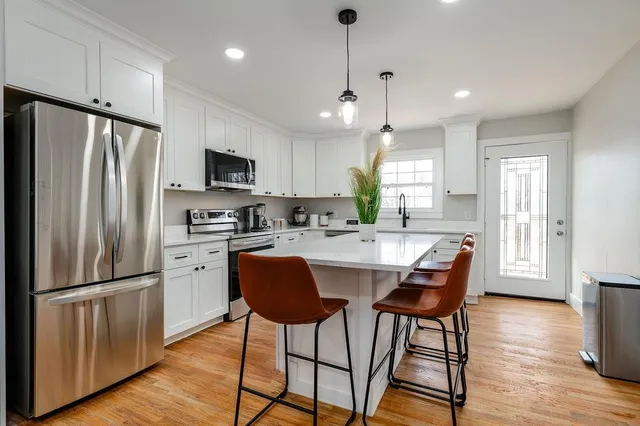 a kitchen with stainless steel appliances granite countertop a refrigerator a microwave a stove a sink dishwasher a dining table and chairs with wooden floor