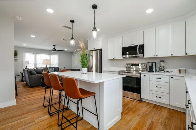 a kitchen with stainless steel appliances kitchen island granite countertop a stove a sink a refrigerator and a dining table with wooden floor