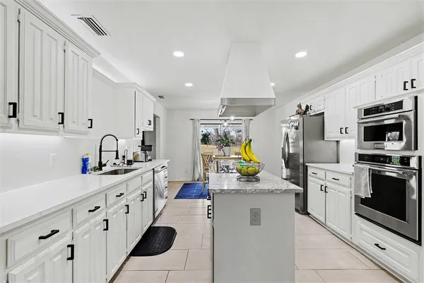 a kitchen that has a lot of white cabinets and stainless steel appliances