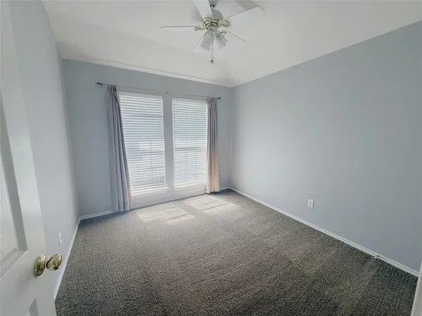 an empty room with chandelier fan and windows