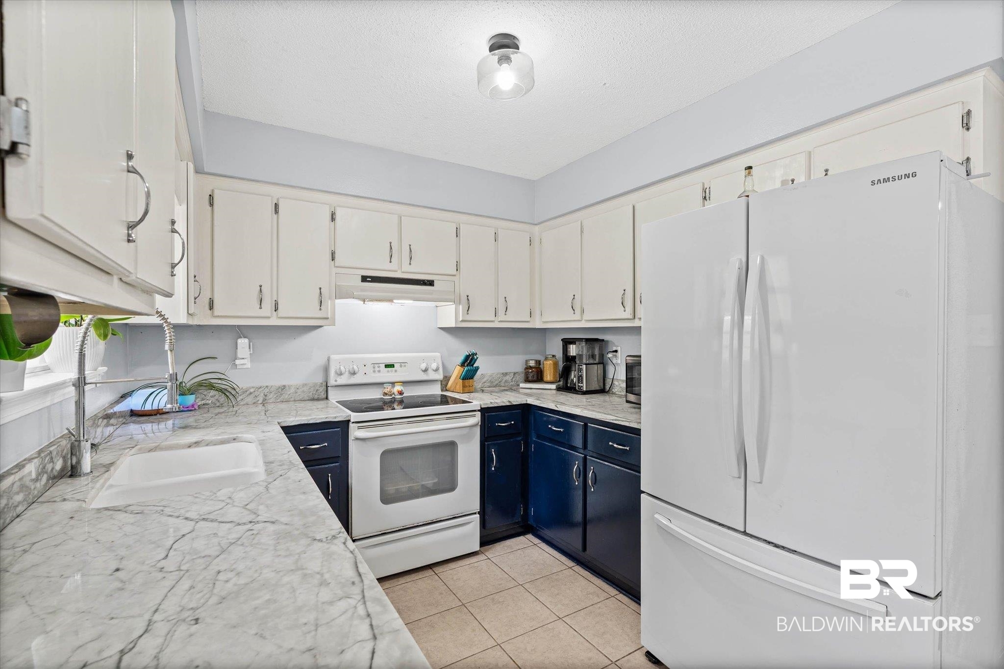 1849 Ranch House Drive Semmes, AL 36575 - Photo 9 of 23 Dual tone kitchen with dual tone cabinetry, white appliances, light tile patterned flooring, light stone counters, and a textured ceiling