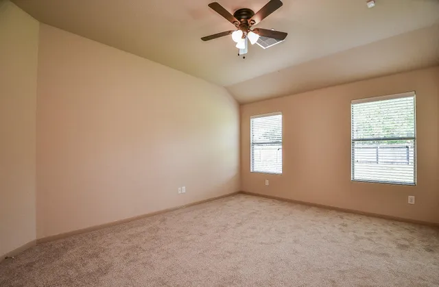 an empty room with chandelier fan and windows