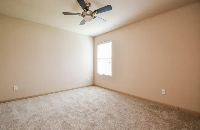 an empty room with a ceiling fan and carpet