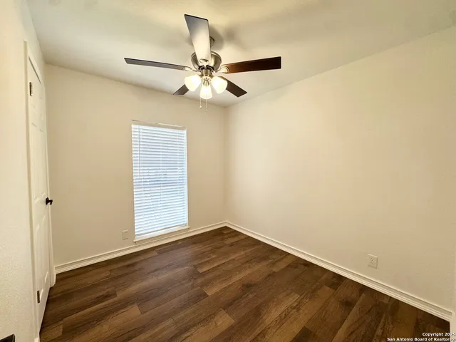 an empty room with wooden floor fan and windows