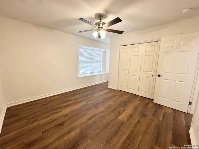 a view of an empty room with wooden floor and a ceiling fan