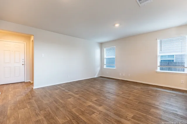 a view of an empty room with wooden floor and a window