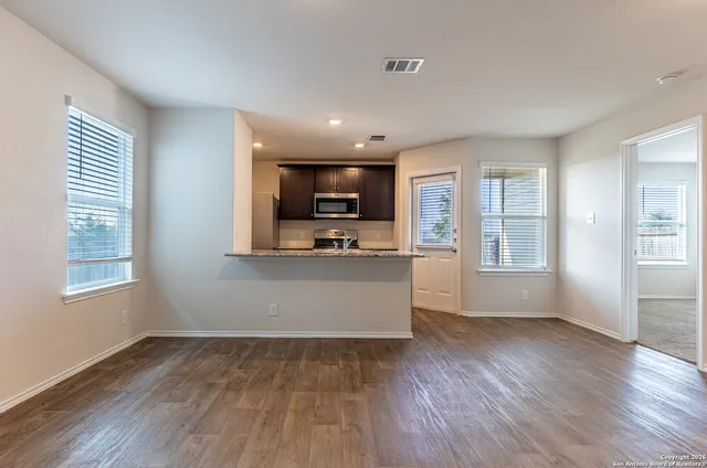 a view of an empty room with kitchen and window