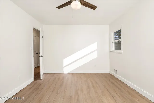 an empty room with wooden floor chandelier fan and windows