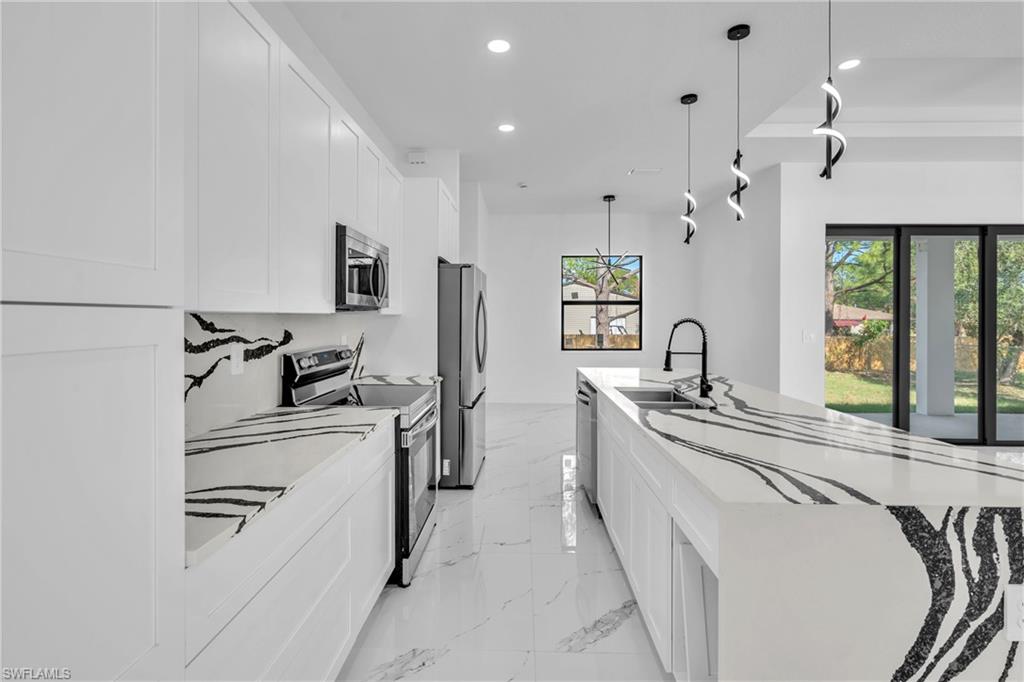 Kitchen featuring stainless steel appliances, light stone countertops, a large island with sink, white cabinetry, and hanging light fixtures