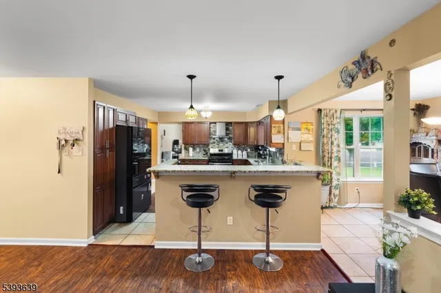 a kitchen with stainless steel appliances kitchen island granite countertop a refrigerator a stove a sink a dining table and chairs with wooden floor