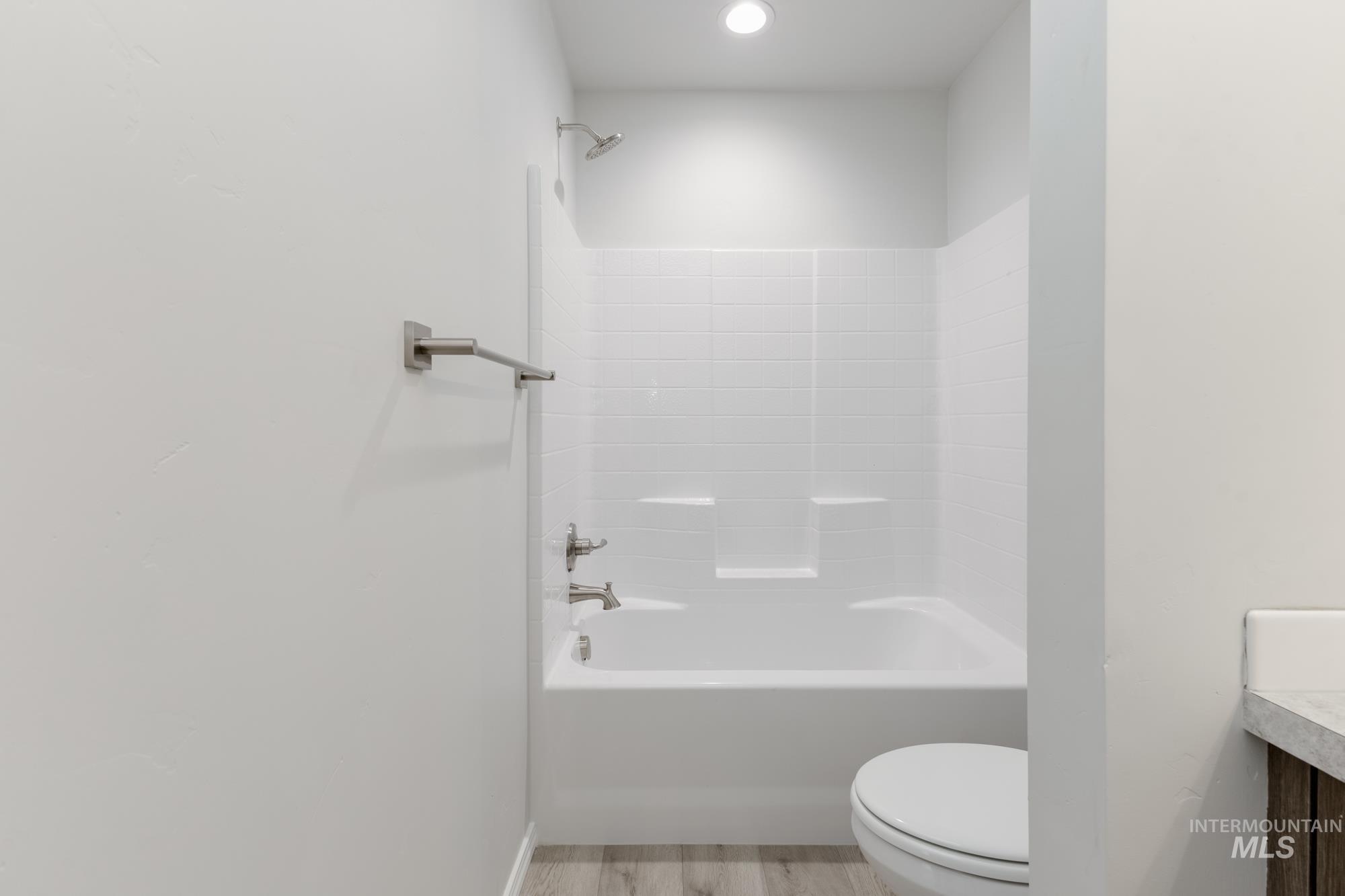12842 Ropers Street Nampa, ID 83651 - Photo 20 of 29 White subway tile shower surround with integrated shelving, brushed nickel fixtures, recessed lighting, and wood-finish flooring
