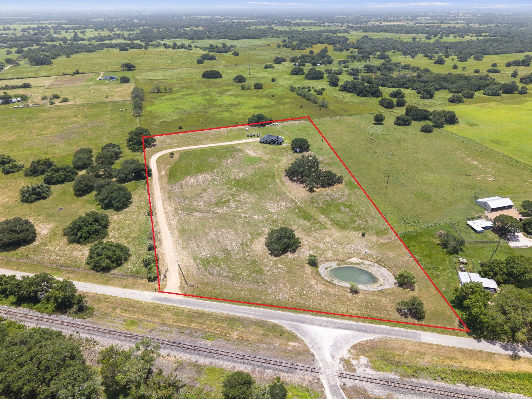 1655 Old Cuero Road Yoakum, TX 77995 - Photo 21 of 24 This aerial view showcases the full extent of the property, highlighting approximately 10 acres of usable land outlined for easy reference. A long private driveway leads to the custom home, offering exceptional privacy and a peaceful country setting. The property features a scenic pond, mature trees, and expansive open pasture with ample space for horses, livestock, recreation, or future additions.