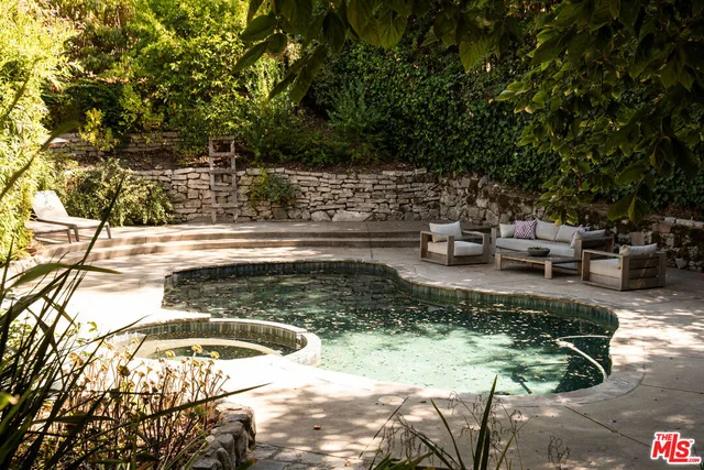 a view of swimming pool with lawn chairs plants and large trees