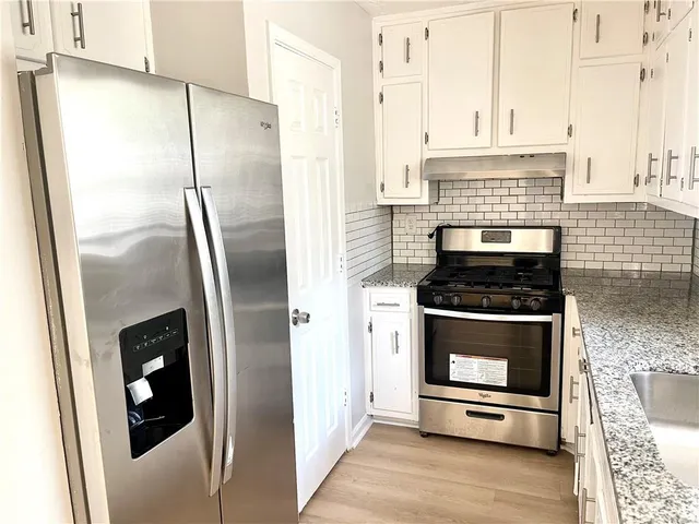 a kitchen with stainless steel appliances granite countertop a refrigerator a stove and a sink with wooden floor