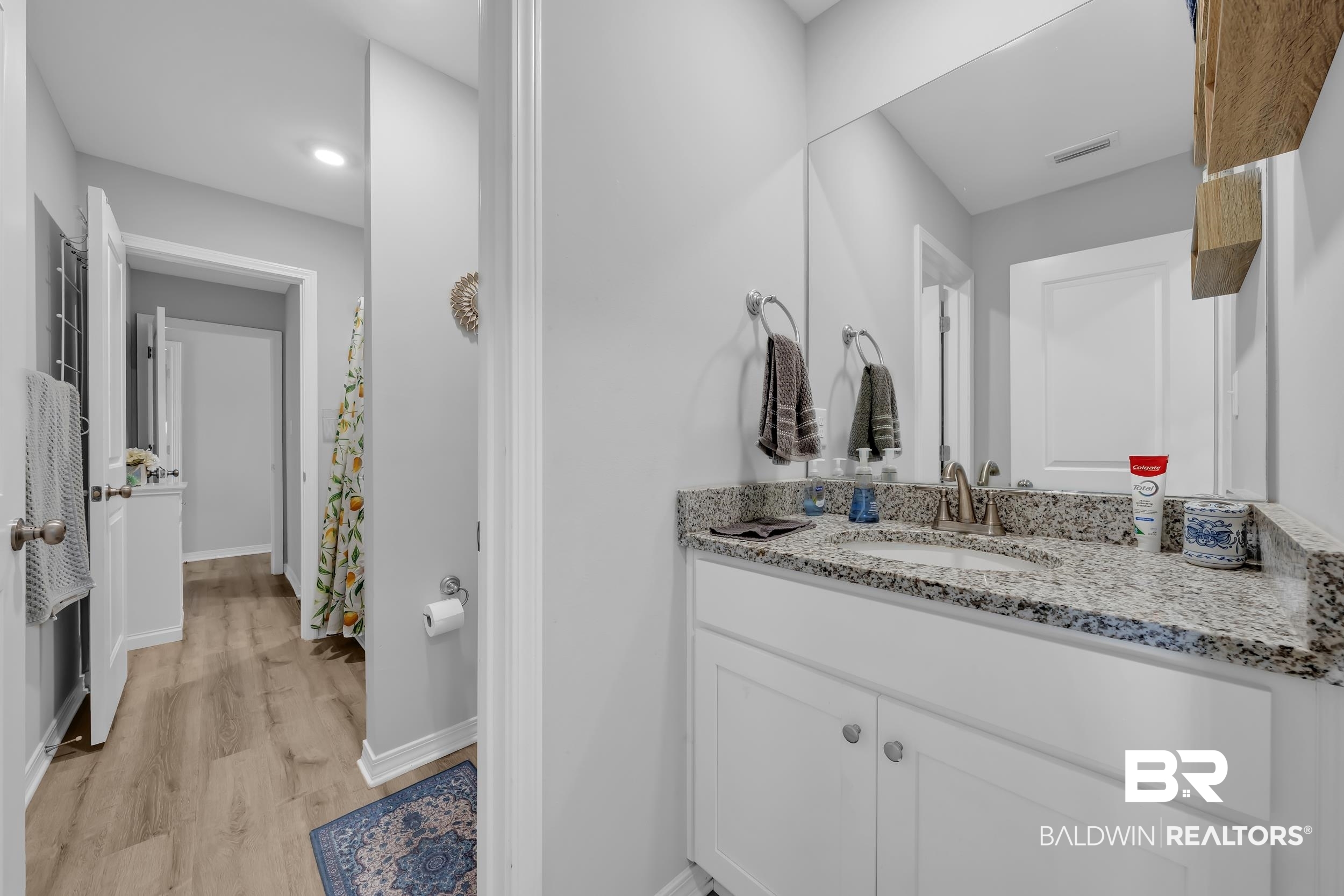 1228 Caper Avenue Foley, AL 36535 - Photo 28 of 54 Bathroom featuring a granite countertop vanity with an undermount sink, a large wall-mounted mirror, white shaker-style cabinetry, and wood-finish flooring