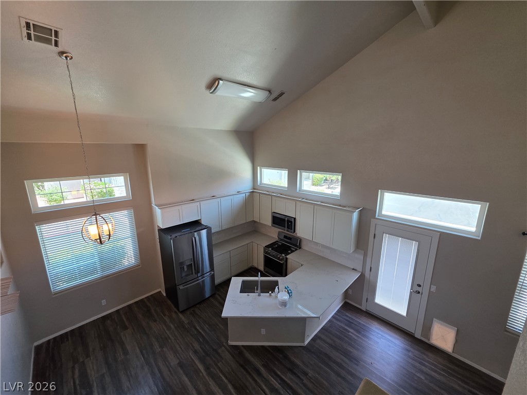 2275 Ramsgate Drive Henderson, NV 89074 - Photo 44 of 84 Lofty ceilings extend above an L-shaped kitchen, well-lit by multiple windows and a statement pendant light.